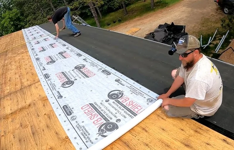 Roofer rolling out protective roof underlayment along the eave of a plywood roof deck
