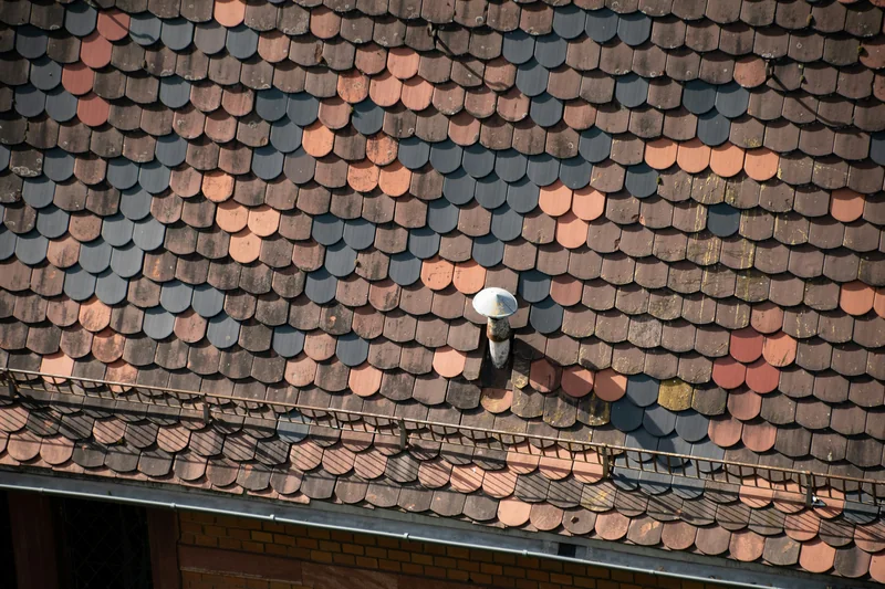 Weathered multicolored roof shingles around a roof vent pipe, a common leak point