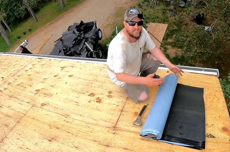 Roofer unrolling synthetic underlayment over a new plywood roof deck