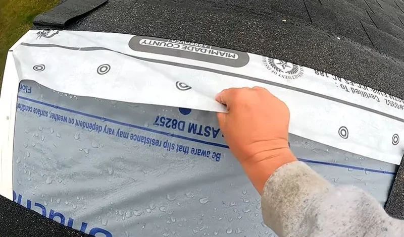 Roofer's hand pressing synthetic underlayment flat during a roof installation