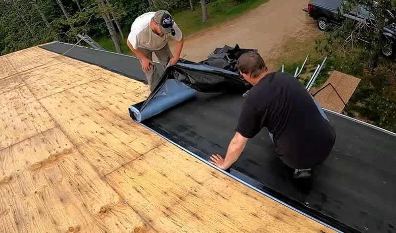 Two roofers rolling out underlayment over new plywood roof decking