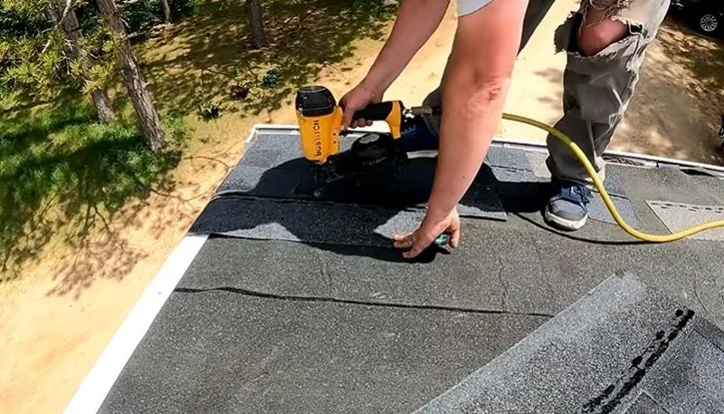 Roofer nailing new architectural shingles along the edge of a roof