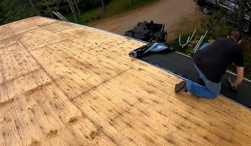 Roofer installing underlayment over a bare plywood roof deck after a full tear-off