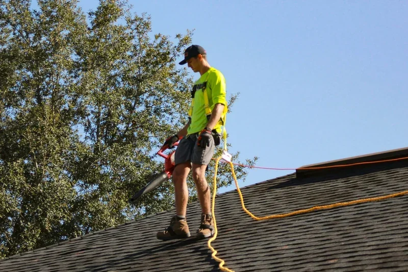 Roofer in a safety harness standing on an asphalt shingle roof during a repair