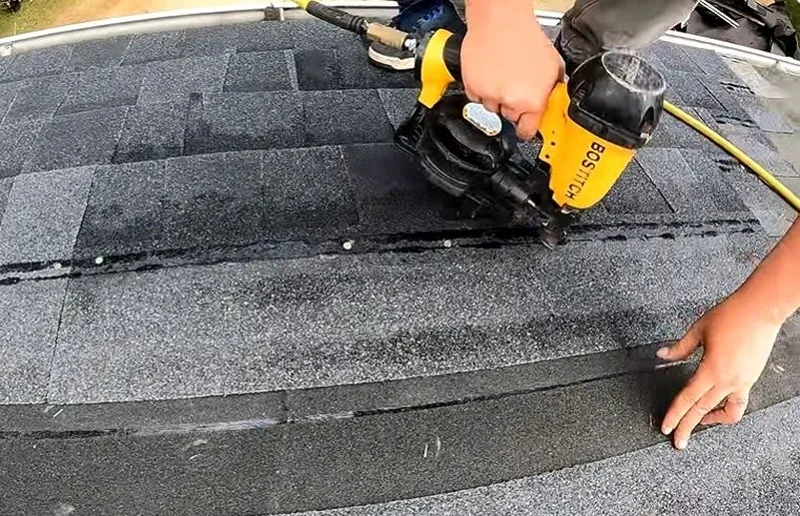Roofer fastening a new course of asphalt shingles with a nail gun
