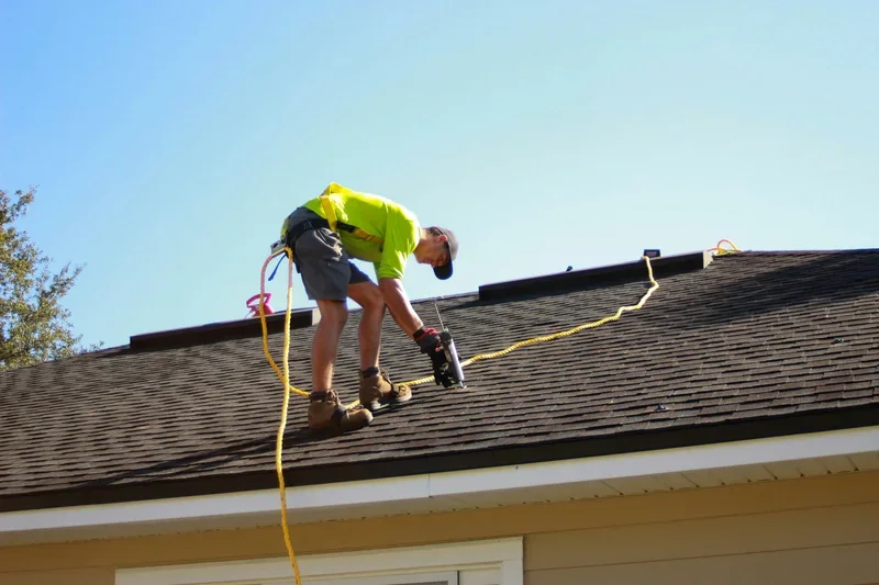 Roofer working along the edge of an asphalt shingle roof with an air hose