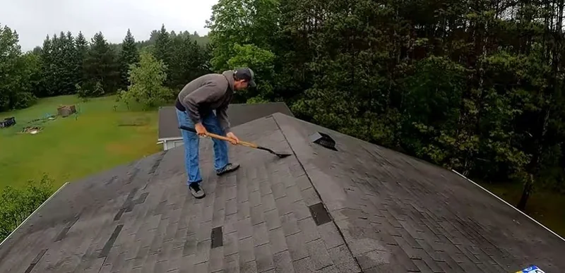 Roofer stripping old asphalt shingles from a pitched roof with a tear-off shovel
