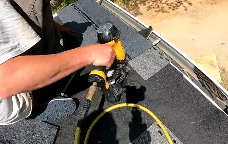 Close-up of a roofer nailing a course of asphalt shingles at the roof edge with a nail gun