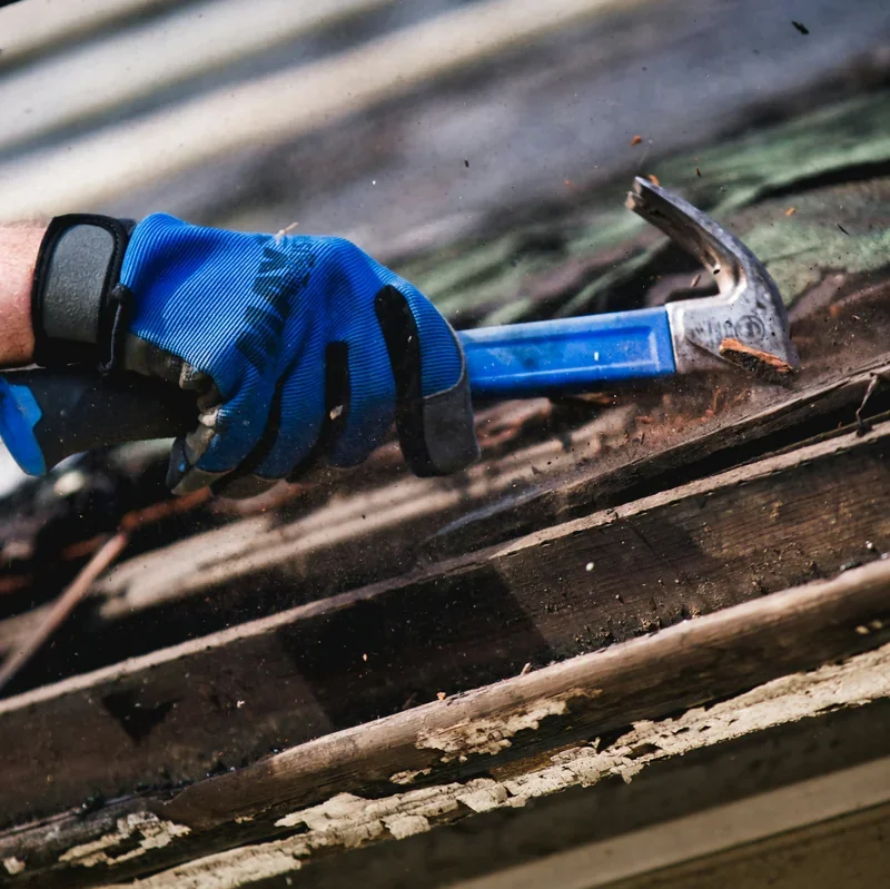 Gloved hand using a hammer to repair a damaged asphalt shingle roof