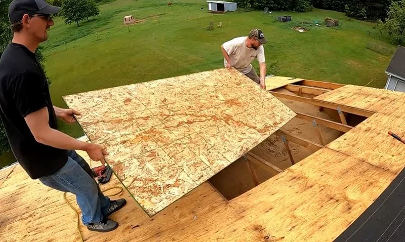 Roofers carrying a new sheet of plywood to replace damaged roof decking
