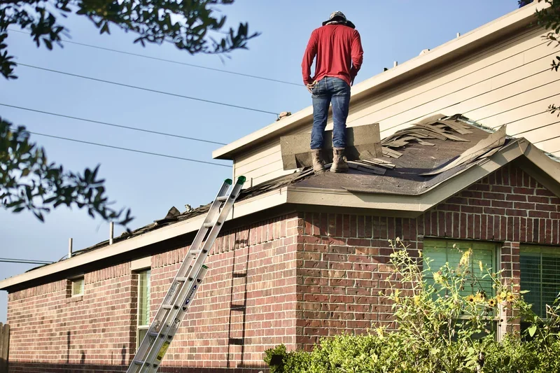 Roofer working on the roof of a brick house with a ladder against the wall